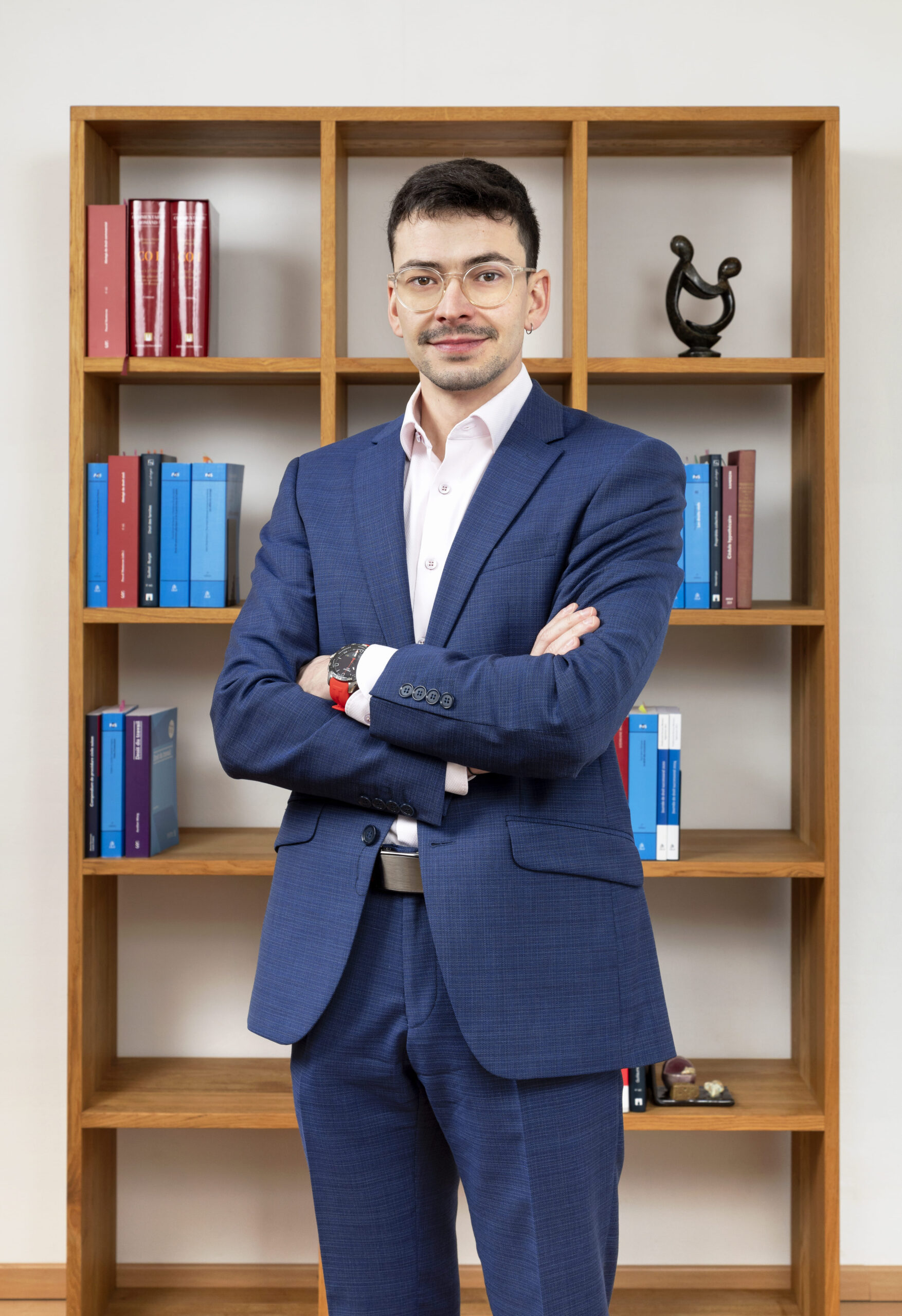 Notaire en costard bleu devant une bibliothèque dans une posture sérieuse.